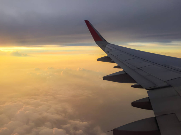 Flughöhe im Passagierjet-Flugzeugflügel, mit wolkenverhangenem, buntem Himmel bei Sonnenuntergang. - Foto, Bild