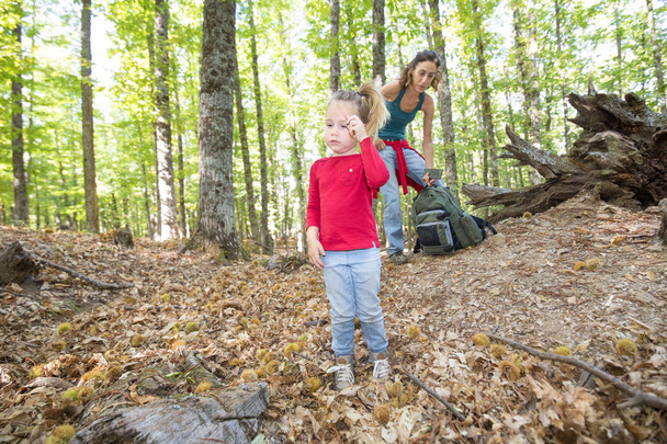 child standing in forest in autumn near mother with backpack - Φωτογραφία, εικόνα