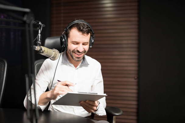 Portret van jonge mannelijke radiopresentator bij radiostation met hoofdtelefoon en microfoon - Foto, afbeelding