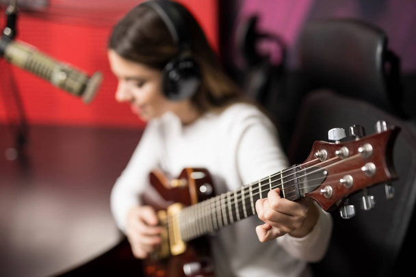Νέος θηλυκός τραγουδιστής παίζει κιθάρα και να τραγουδάει στο μικρόφωνο στο ραδιοφωνικό σταθμό  - Φωτογραφία, εικόνα