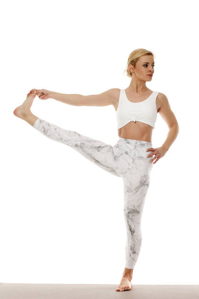 Yoga, sport, training en lifestyle concept - jonge blonde vrouw doen yoga oefening. Portret van een jonge mooie vrouw in witte sportkleding doen yoga praktijk. Staande pose. - Foto, afbeelding