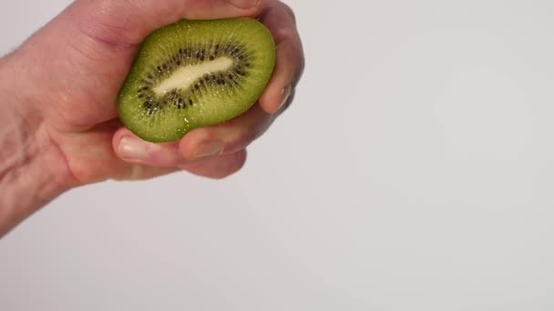 hand squeezes the juice from the kiwi into a glass on a white background - Кадри, відео