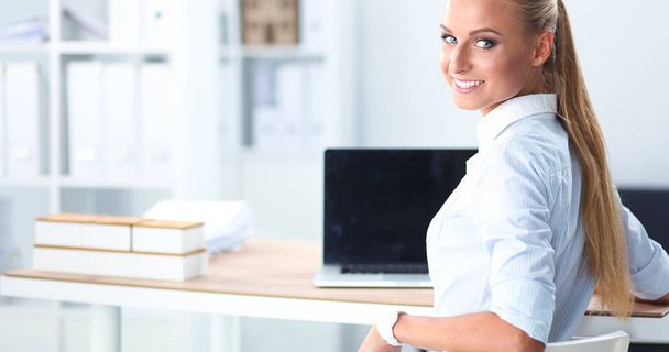 Attractive businesswoman sitting on a desk with laptop in the office - Fotó, kép