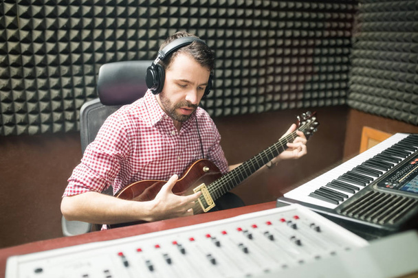 Hispanic guitarist in soundproof recording room playing guitar and composing music - Valokuva, kuva