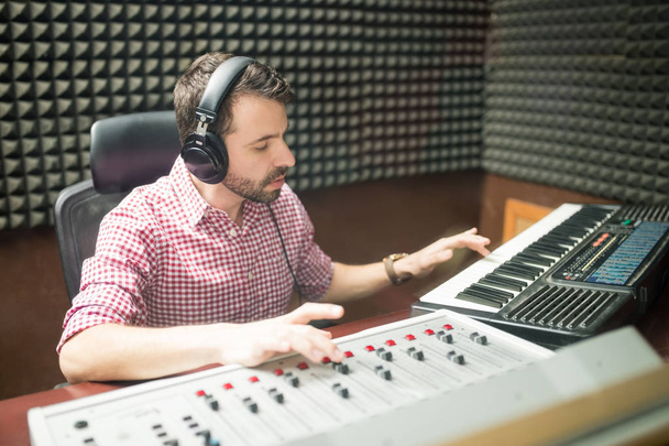 звукоинженер, работающий с музыкальной клавиатурой и панелью смешивания в звукоизолированной студии
 - Фото, изображение