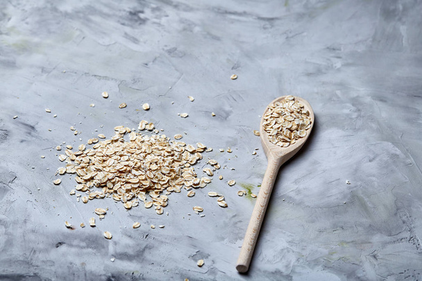 Wooden spoon and heap of oats on white textured background, copy space, top view, close-up, selective focus - Photo, image