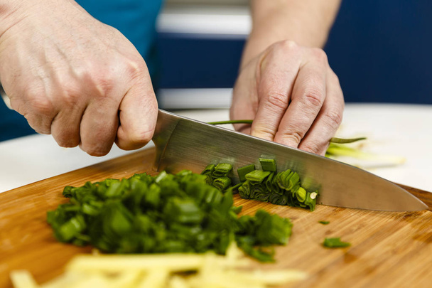 Man chopping spring onions on a wooden board, closeup shot - Photo, Image