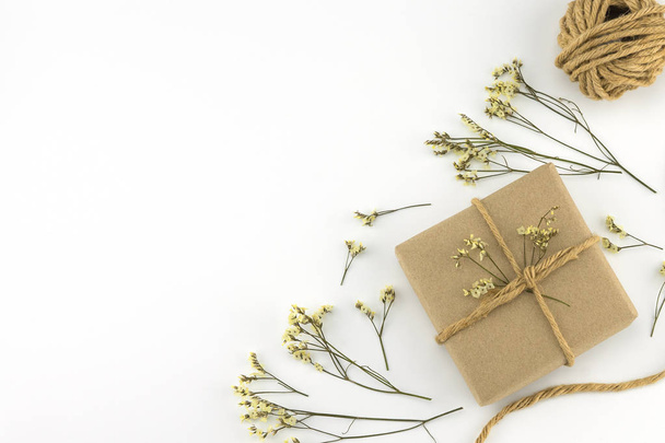 Bruin geschenkdozen en touw met gele limonium caspia bloemen op witte houten achtergrond met kopie ruimte - Foto, afbeelding