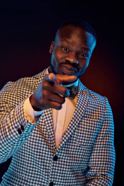 Neon portrait of handsome black man in white shirt and plaid jacket with floral bow tie mocking finger at you. - Foto, Imagen