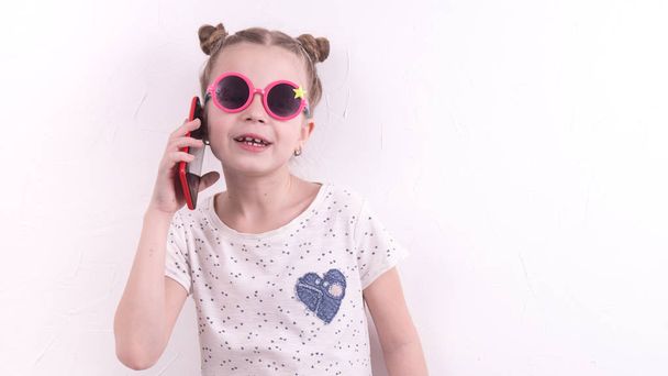 Communication technologies: A girl in pink glasses emotionally talks on the red phone. - Fotó, kép