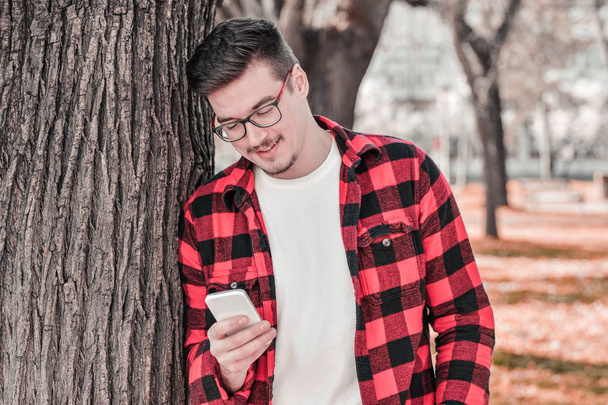 Outdoor portrait of modern young man with mobile phone in park - Photo, Image