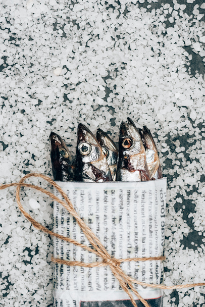 Top view of pile of fish in newspaper wrapped by string on surface covered by salt  - 写真・画像