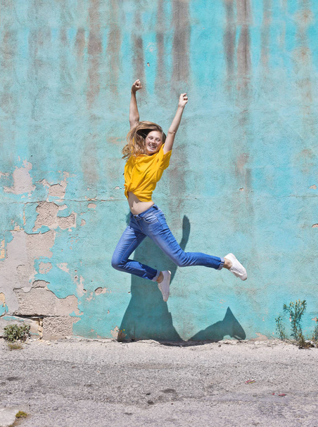 Girl jumping on front of a blue wall - 写真・画像