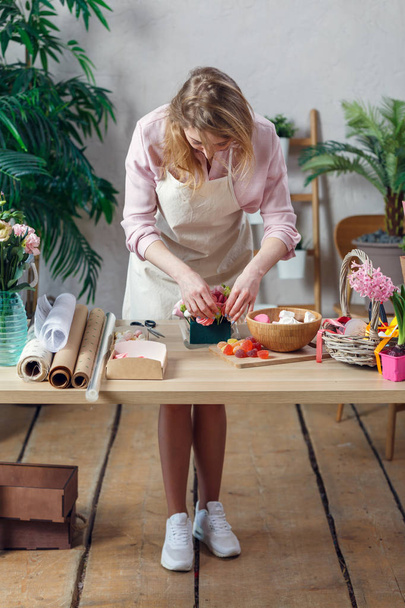 Picture of florist woman in apron with marshmallow, marmalade at table - Photo, image