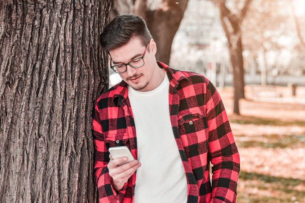 Outdoor portrait of modern young man with mobile phone in park - Photo, Image