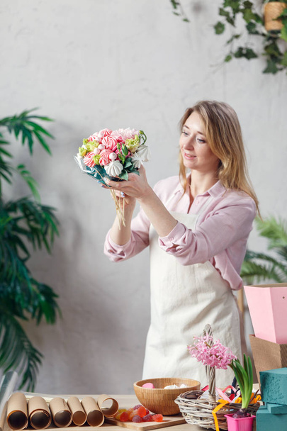Picture of florist holding bouquet in hands at table with marmalade, marshmallow, boxes, paper - Foto, imagen