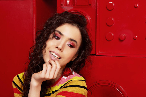 Studio fashion shooting. The girl in a bright outfit, top and pants flared in red and orange colors. Brunette with curly hair. Close-up portrait. Brown eye - Foto, Imagem