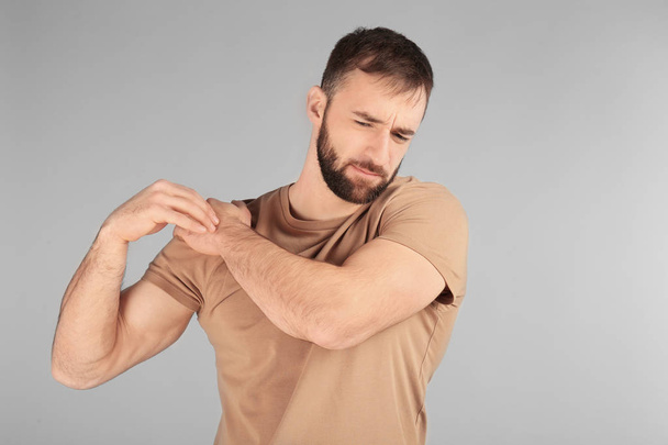 Young man suffering from pain in shoulder on light background - Foto, imagen