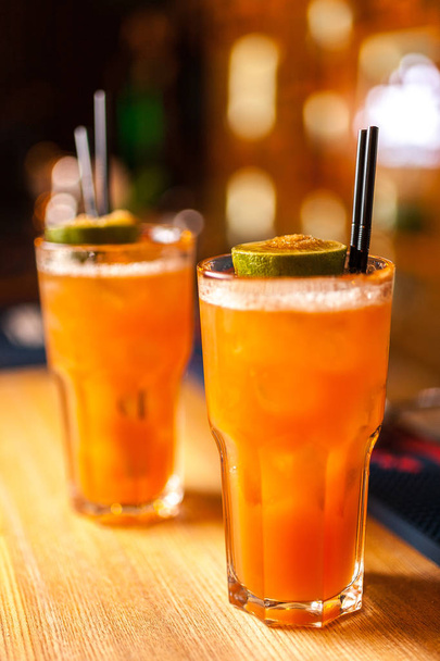 Detail ze dvou barevné oranžový koktejl s limetkou a hnědý cukr v baru, rozmazané pozadí. - Fotografie, Obrázek