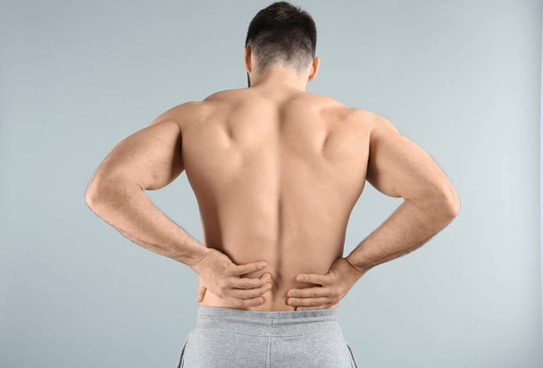 Young man suffering from back pain on light background - Fotoğraf, Görsel