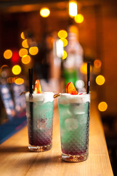 Twee blauwe cocktails met citroen op de balk, onscherpe achtergrond. - Foto, afbeelding