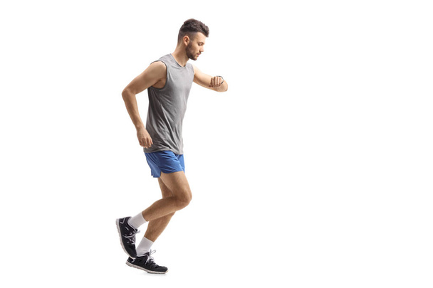 Full length profile shot of an athletic guy running and looking at his watch isolated on white background - Zdjęcie, obraz