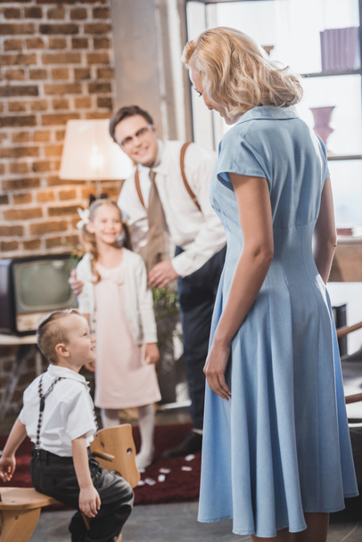 happy 1950s man and kids looking at beautiful woman in blue dress at home - Фото, изображение