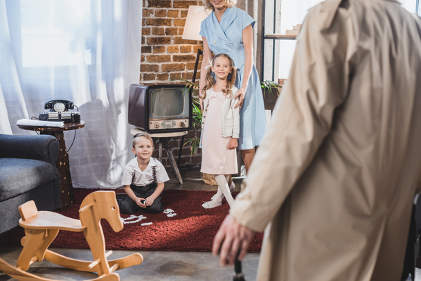 обрезанный снимок отца, возвращающегося домой и смотрящего на счастливую семью, играющую дома, в стиле 1950-х годов
 - Фото, изображение