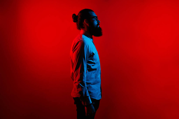 Abstract side view of bearded hipster man in casual with long hair and wearing eyeglasses standing over red background. Profile portrait. - Fotó, kép