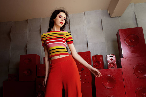 Studio fashion shooting. The girl in a bright outfit, top and pants flared in red and orange colors.Brunette with curly hair dancing - Photo, image