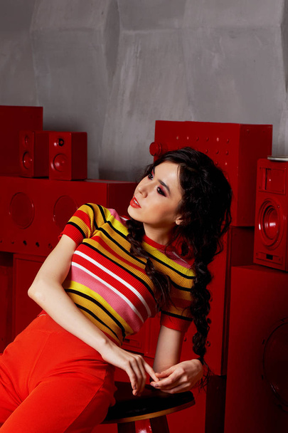 Studio fashion shooting.The girl in a bright outfit, top and pants flared in red and orange colors. Brunette with curly hair - Φωτογραφία, εικόνα