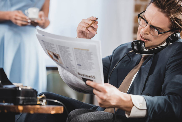 ο άνθρωπος στο κοστούμι διαβάζοντας εφημερίδα και μιλάμε vintage τηλεφωνικά - Φωτογραφία, εικόνα
