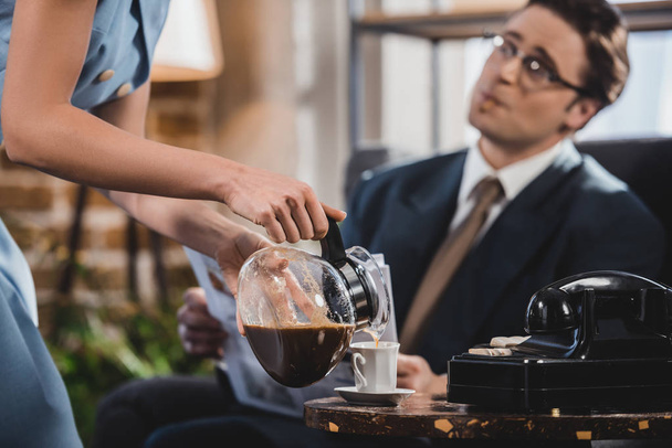 cropped shot of woman pouring coffee to husband in suit reading newspaper, 1950s style - Photo, Image