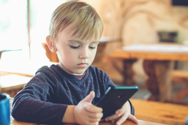 Cute little boy playing games on smartphone at home. - Zdjęcie, obraz