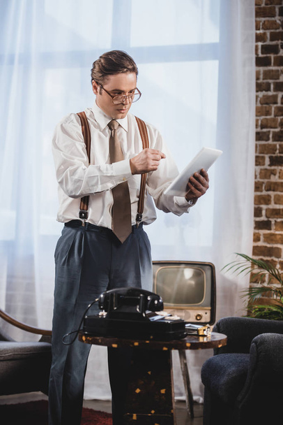 retro styled man in eyeglasses using digital tablet at home - 写真・画像