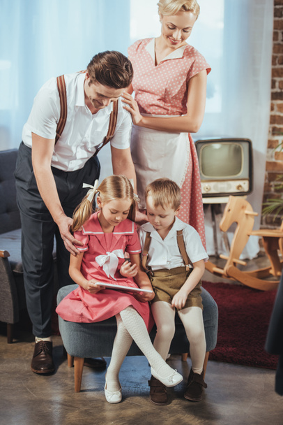 happy parents looking at cute little kids using digital tablet, 1950s style  - Фото, изображение