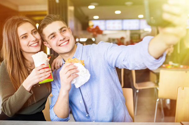 Happy smiling woman and a handsome man are enjoying their delicious and tasty burgers and doner taking selfie phone - Foto, immagini