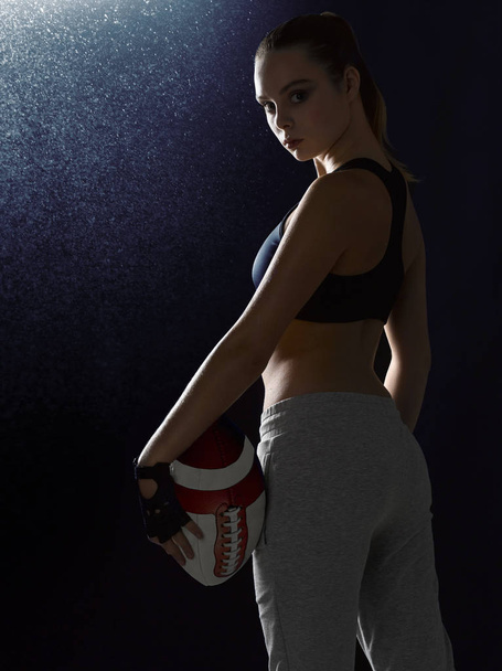 Ένα κορίτσι σε ένα κοστούμι αθλητισμού στέκεται με μια μπάλα. - Φωτογραφία, εικόνα