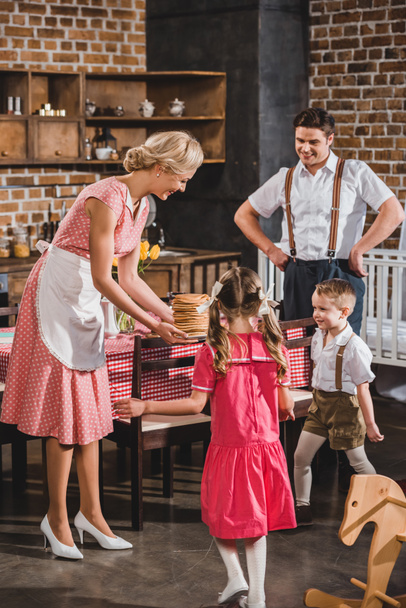 kinderen en man kijken lachende vrouw bedrijf heerlijke pannenkoeken, stijl van de jaren 1950 - Foto, afbeelding