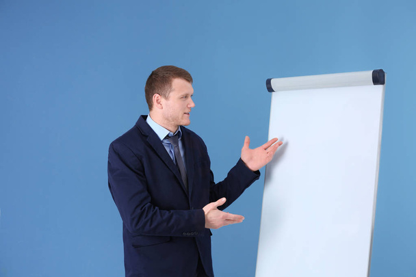 Business trainer giving presentation on flip chart board against color background - Fotoğraf, Görsel