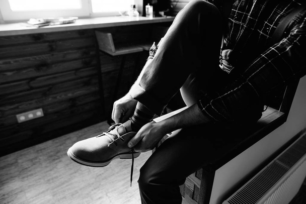 若い男が坐っている間彼の靴に置く - 写真・画像