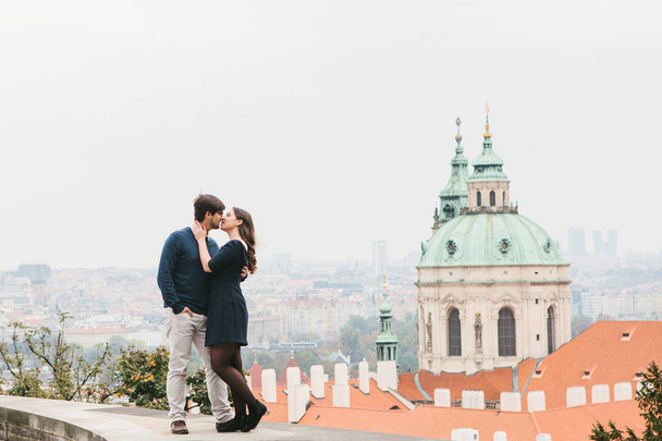 愛する若い美しいカップル ヨーロッパ抱擁とキスをチェコ共和国のプラハの美しい景色の背景からの学生。近い感情や人々 の間の感情. - 写真・画像