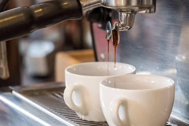 Espresso dripping from portafilter of coffee machine into white cup - Foto, Bild