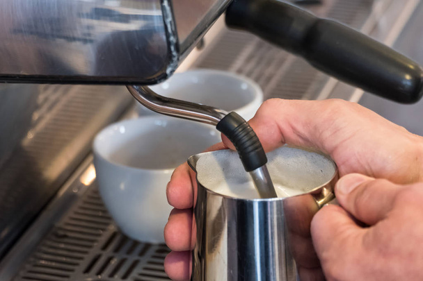 Steaming and frothing milk in tumbler for cappuccino or latte - 写真・画像