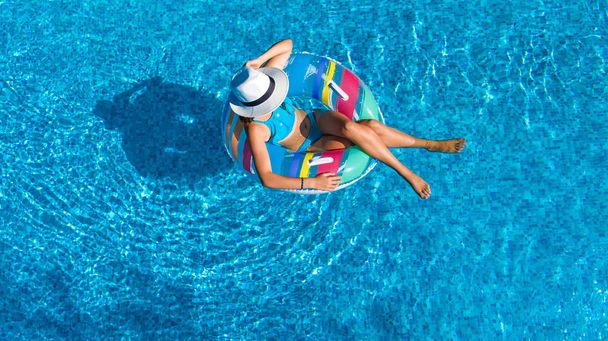 Aerial top view of beautiful girl in swimming pool from above, relax swim on inflatable ring donut and has fun in water on family vacation, tropical holiday resort - Φωτογραφία, εικόνα