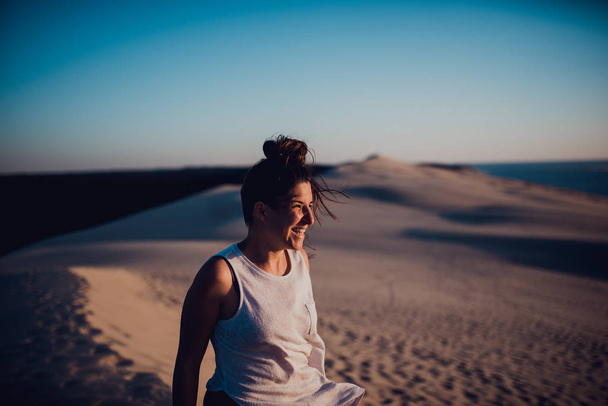 Vista lateral de la mujer de pie en las dunas de arena y disfrutar del sol
. - Foto, Imagen