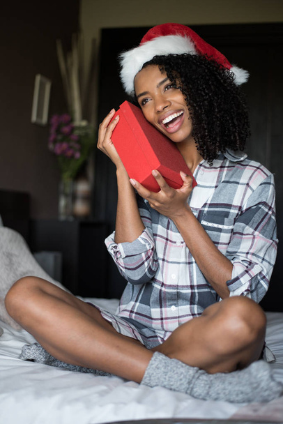 schöne süße schwarze junge Frau im Pyjama auf dem Bett mit Weihnachten - Foto, Bild