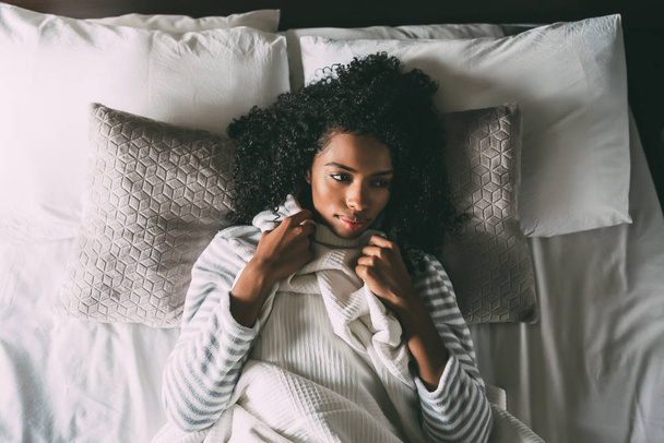 Красивая задумчивая черная женщина с кудрявыми волосами, лежащая на кровати и смотрящая в сторону
 - Фото, изображение