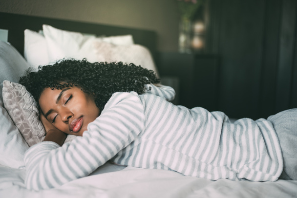 крупный план симпатичной черной женщины с кудрявыми волосами, спящей в постели с закрытыми глазами
 - Фото, изображение