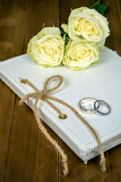 пара обручок на білому журналі з струнним бантом і трояндовим букетом
 - Фото, зображення